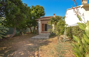 Ein Wohnhaus mit befestigter Auffahrt, einer Holztür und einem kleinen Garten mit unterschiedlichen Pflanzen.