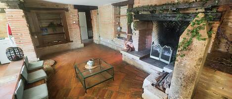 Una habitación acogedora con una chimenea de ladrillo, una mesa de centro de vidrio y un rincón de descanso con sillones mullidos.