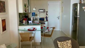 A modern kitchen with white cabinets, a microwave, and a toaster. There is a dining area with a glass table and chairs.
