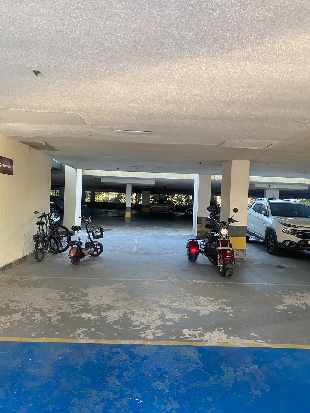 A parking garage with concrete pillars, a blue line marking, and vehicles including a motorcycle and a car.