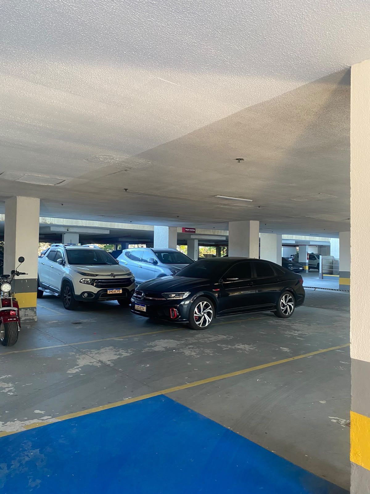 Um estacionamento com vários carros estacionados, incluindo um SUV branco e um sedan preto.