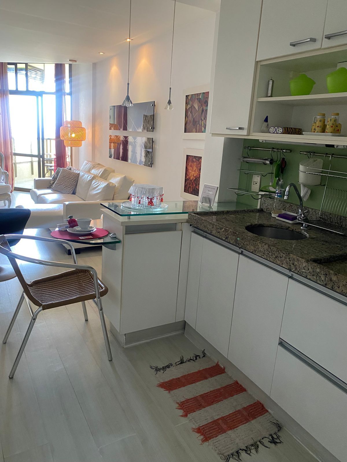 Cozinha moderna com ilha central, sala de jantar com sofá e cadeiras, e sala de estar com sofá e mesa de centro.