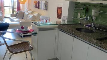 Cozinha moderna com ilha central, sala de jantar com sofá e cadeiras, e sala de estar com sofá e mesa de centro.