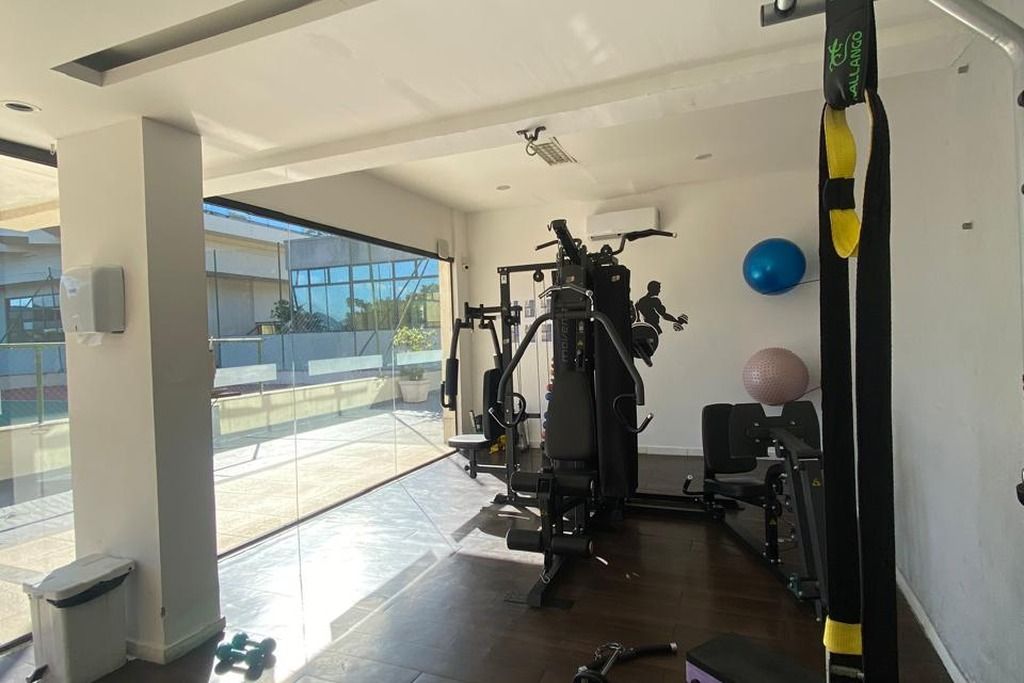 Academia com equipamentos de ginástica, uma grande janela e vista para o exterior.