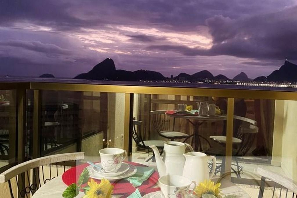A balcony with a table set for tea, overlooking a cityscape with mountains in the background.