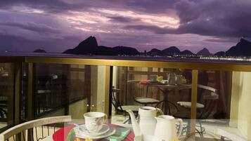A balcony with a table set for tea, overlooking a cityscape with mountains in the background.