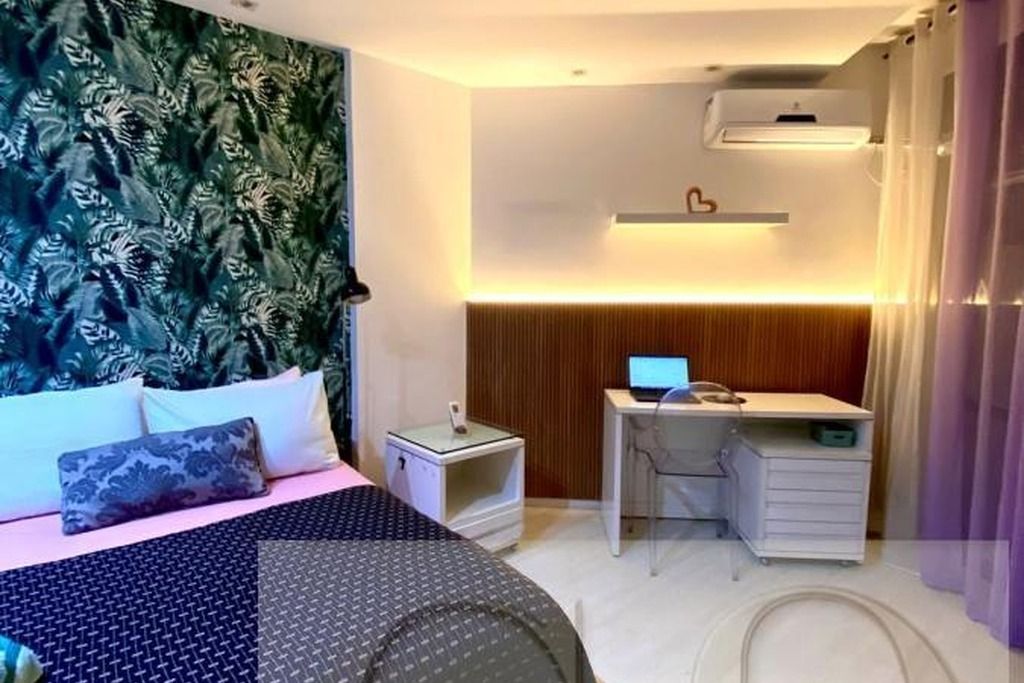 A bedroom with a bed, a desk, a chair, an air conditioner, and a wall-mounted shelf.