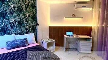 A bedroom with a bed, a desk, a chair, an air conditioner, and a wall-mounted shelf.