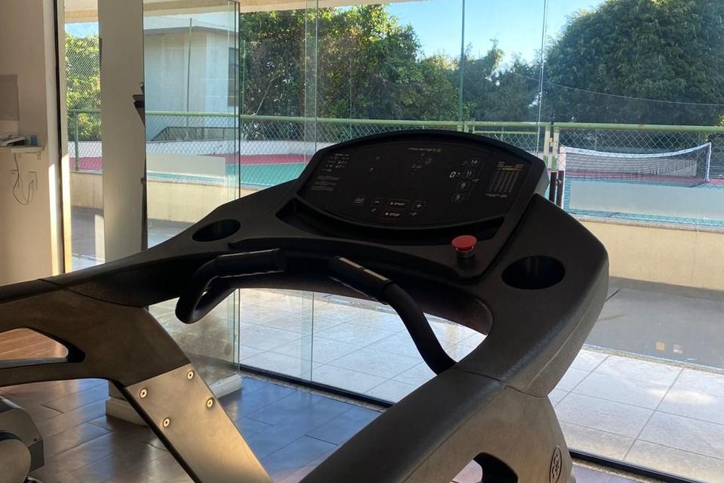 A stationary bike with a digital display, positioned indoors with a view of an outdoor tennis court through a glass door.