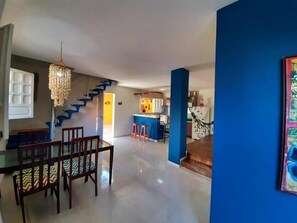 Àmplia zona d'estar amb una escala, una taula de dinar amb cadires i una cuina al fons.