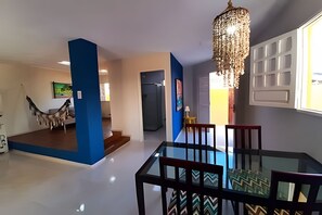 A modern interior with a dining area featuring a glass table and chairs, a chandelier, and a view of a building outside. - Porto de Galinhas Maraca 100mMar Loctemp (Ipojuca)