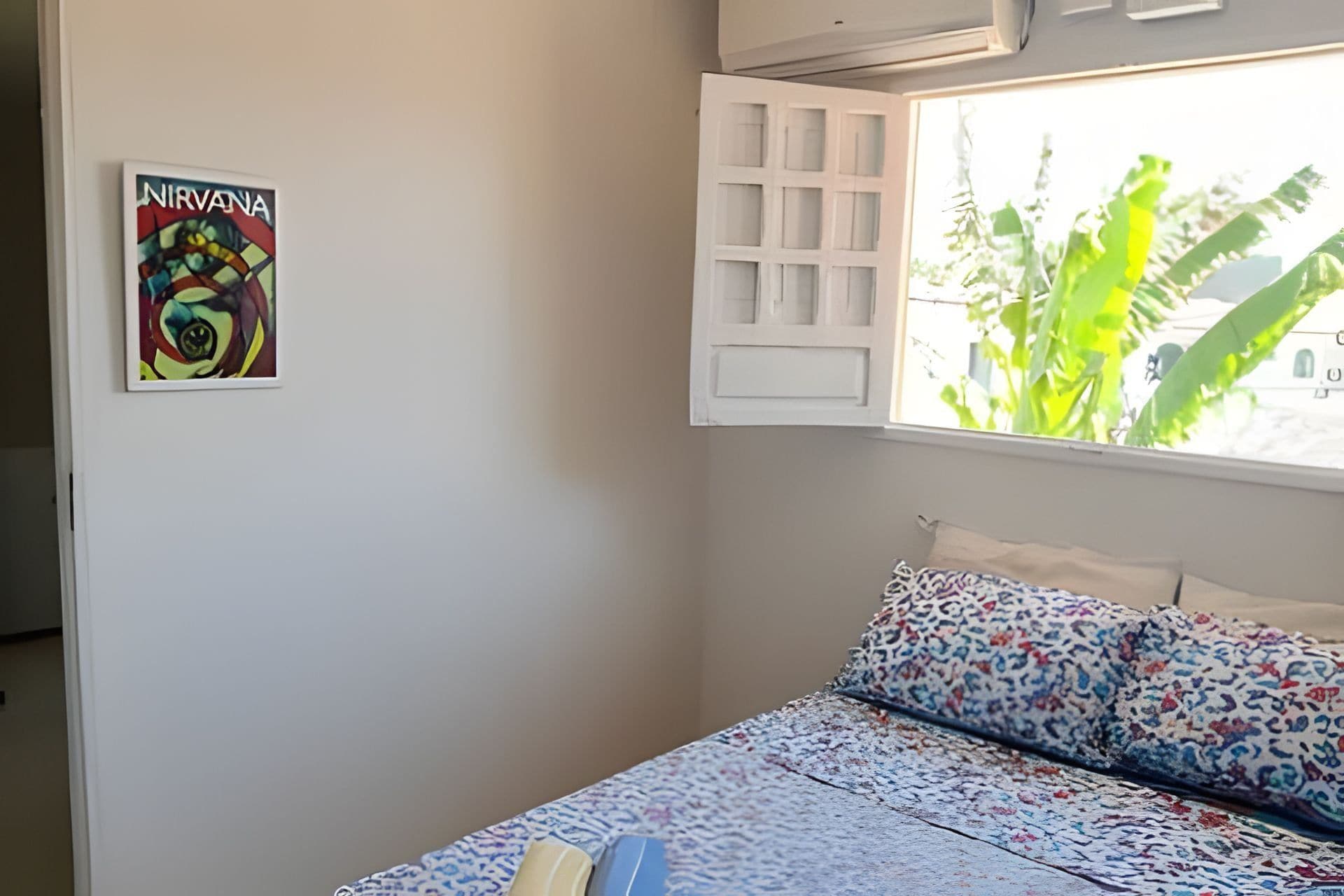 A bedroom with a bed, a window with a view of greenery, and a wall with a framed picture.