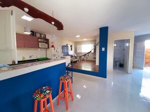 Zona de estar àmplia amb cuina, cadira de l'aire i dos tamborets colorits.