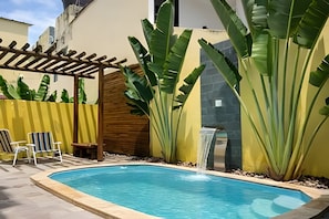 A swimming pool with a wooden pergola, two lounge chairs, and large banana plants. - Porto de Galinhas Maraca 100mMar Loctemp (Ipojuca)