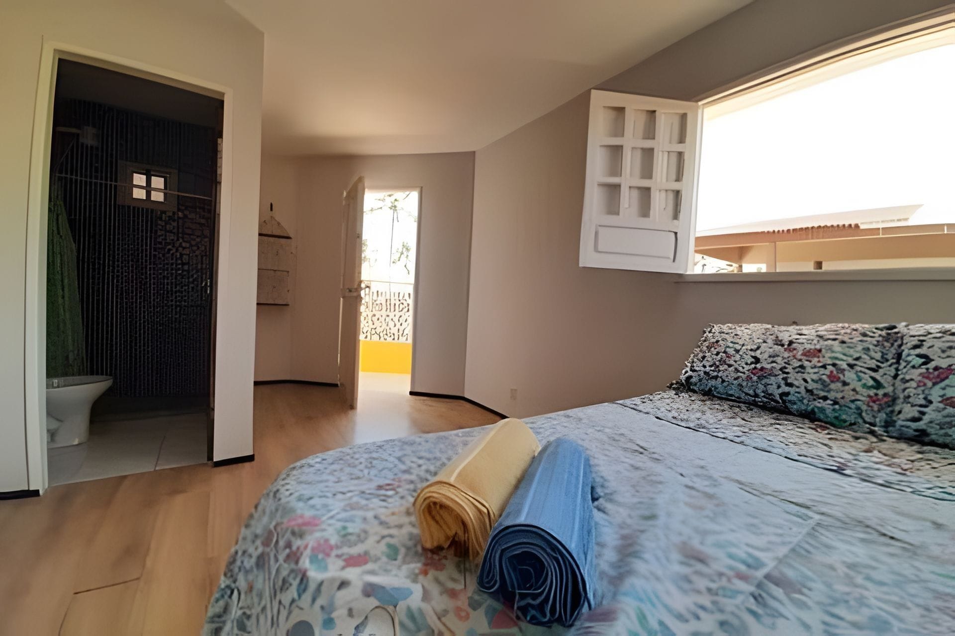 A bedroom with a bed, a window, a door, and a view of the outside.