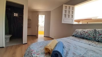 A bedroom with a bed, a window, a door, and a view of the outside.