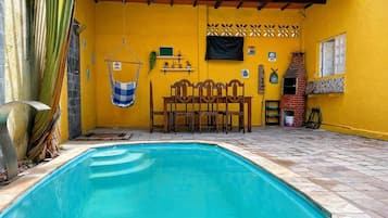 A swimming pool with a tiled deck, a wooden bench, and a hanging chair.