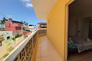 A balcony with a tiled floor, a bed with a patterned bedspread, and a view of neighboring buildings. - Porto de Galinhas Maraca 100mMar Loctemp (Ipojuca)