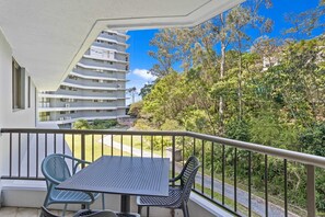 A balcony with a table and chairs, overlooking a residential building and a lush green area. - Burleigh Headland 2 Bedroom Stay (Gold Coast City)