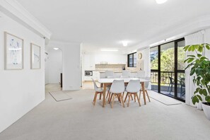 Cocina moderna con armarios blancos, una mesa de comedor con sillas y un ventanal con vista a la vegetación.