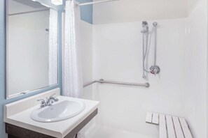 A bathroom with a white sink, a mirror, a shower with a handheld showerhead, and a grab bar. - Room in Irving (Irving)