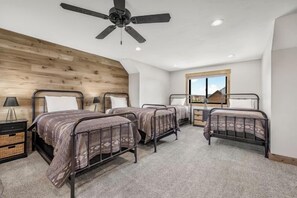 Quarto com quatro beliches de metal, ventilador de teto e uma grande janela com vista para as montanhas.