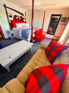 Ein Hotelzimmer mit Himmelbett, einer Couch mit roten und schwarzen Kissen, einem weißen Couchtisch und einem roten Sessel.