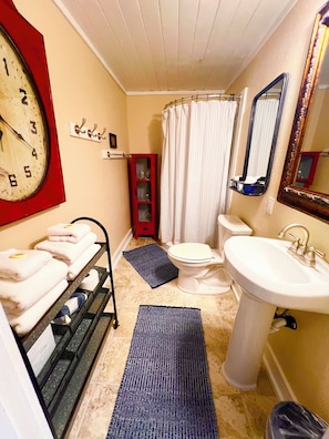 Ein Badezimmer mit Waschbecken, Toilette, Duschvorhang und einer Uhr an der Wand.