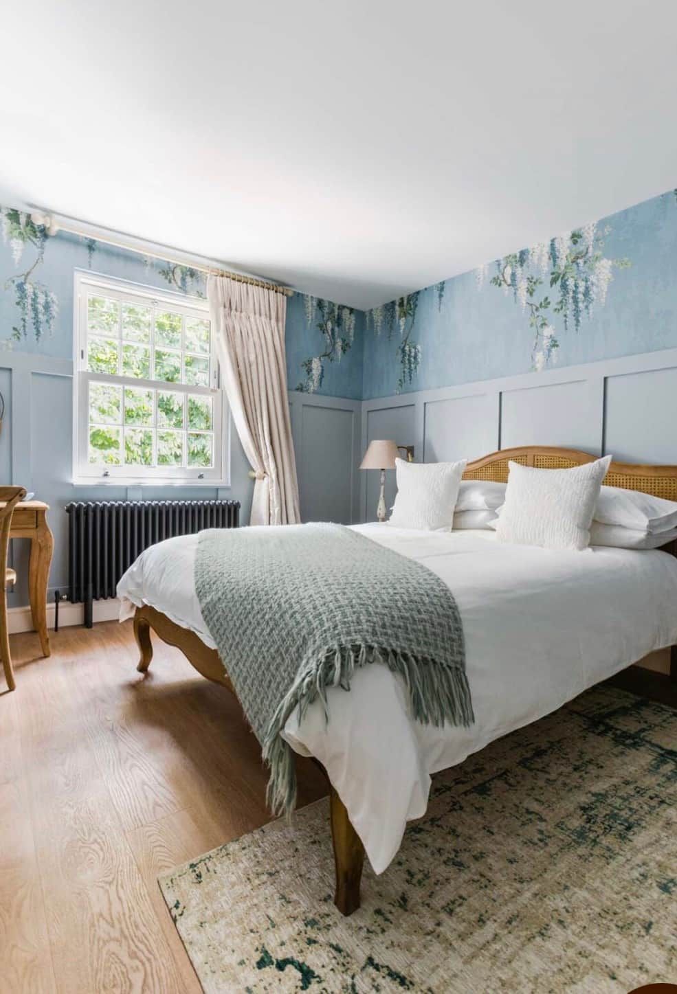 A bedroom with a bed, a window with curtains, a radiator, and a wooden floor.