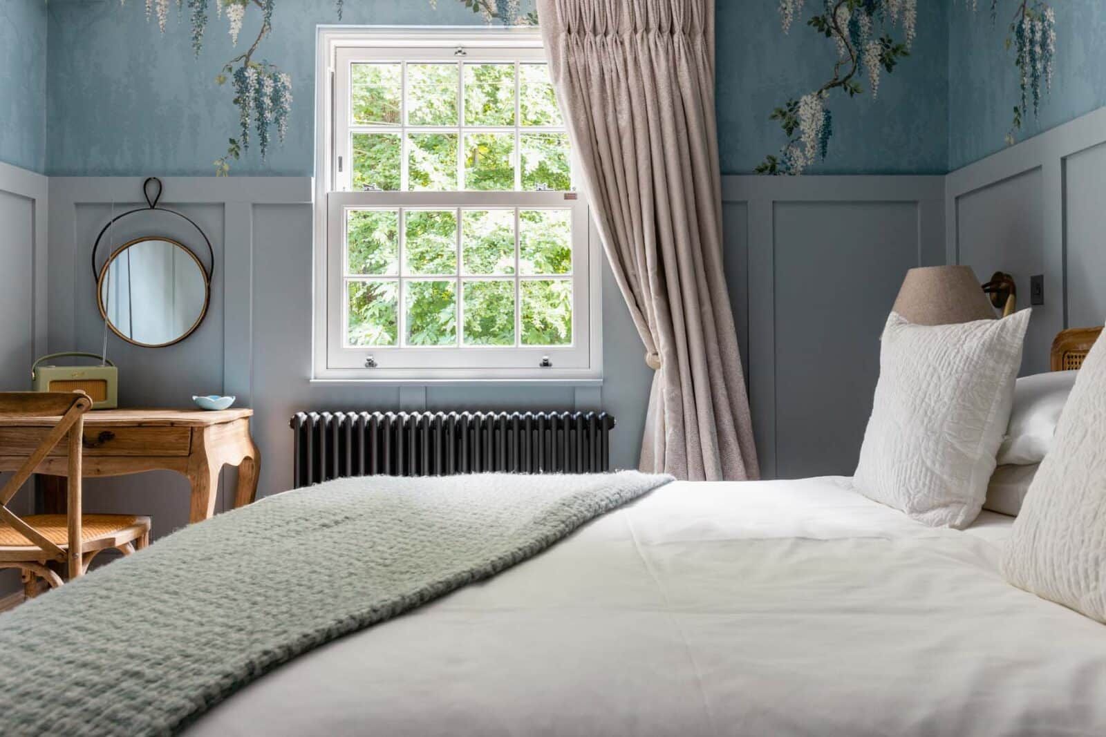A bedroom with a bed, a dresser, a mirror, a radiator, and a window with curtains.
