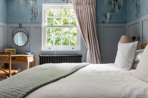 Ein Schlafzimmer mit einem Bett, einem Schminktisch, einem Spiegel, einer Heizung und einem Fenster mit Vorhängen.