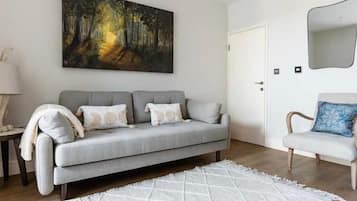 Ein Wohnzimmer mit einem grauen Sofa, einem weißen Teppich und einem Gemälde von einem Wald.