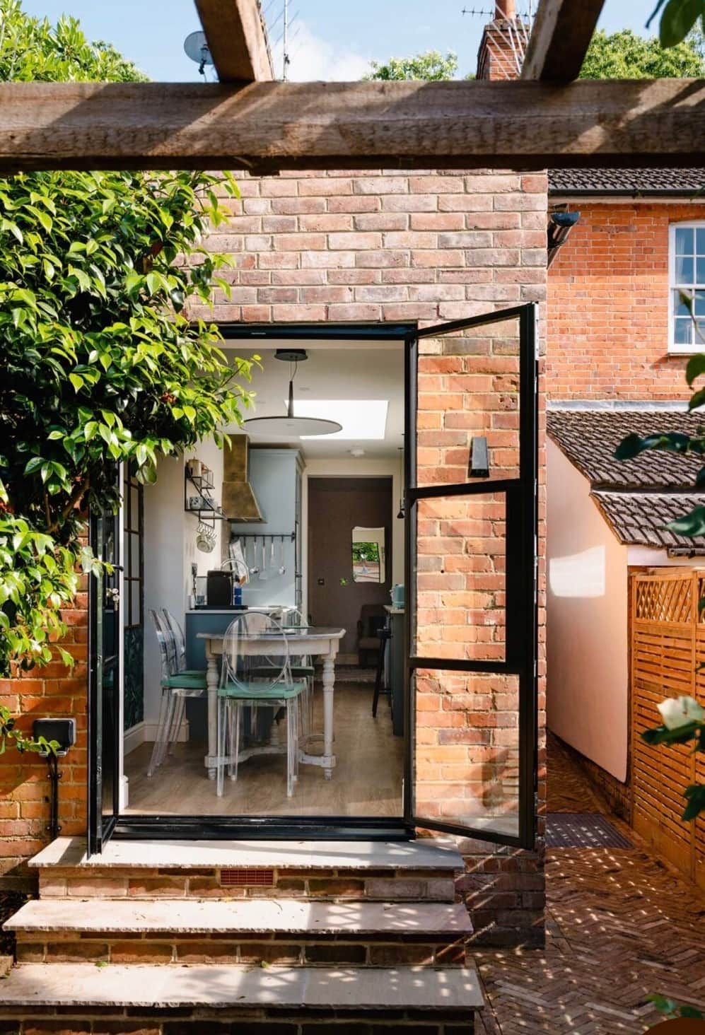 A brick house with a glass door leading to a dining area with a table and chairs.