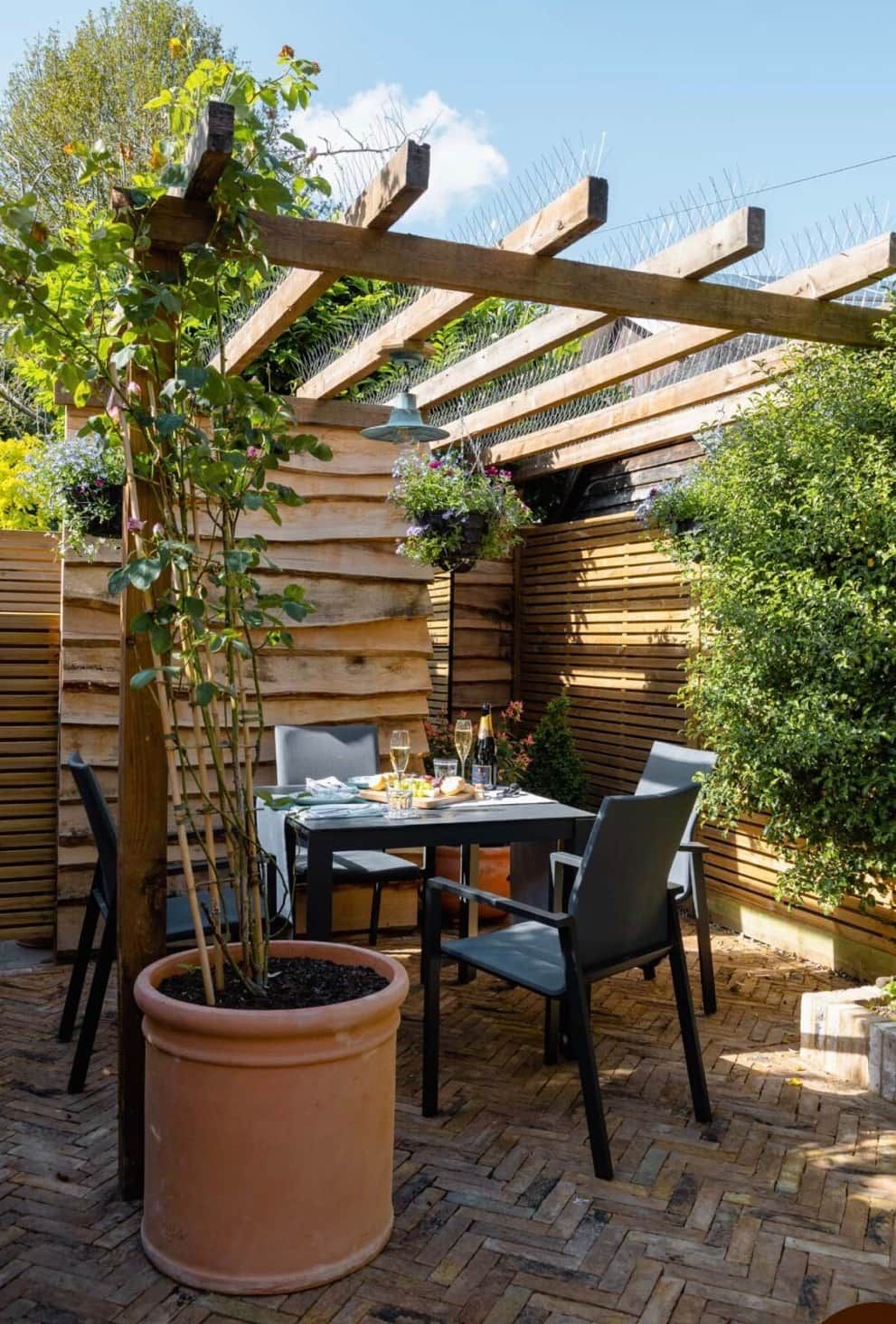 Eine Außenpatio mit einer Holz-Pergola, einem Tisch mit Stühlen und einem Blumentopf.