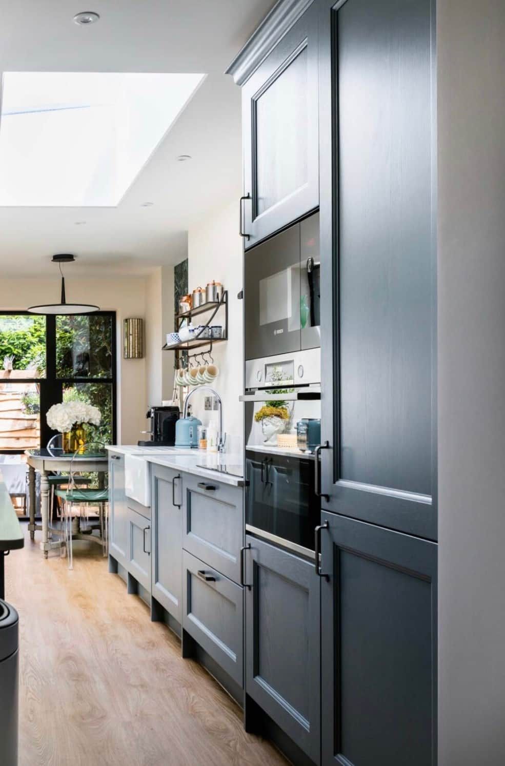 A modern kitchen with built-in appliances, a dining area with a table and chairs, and a view of greenery outside.