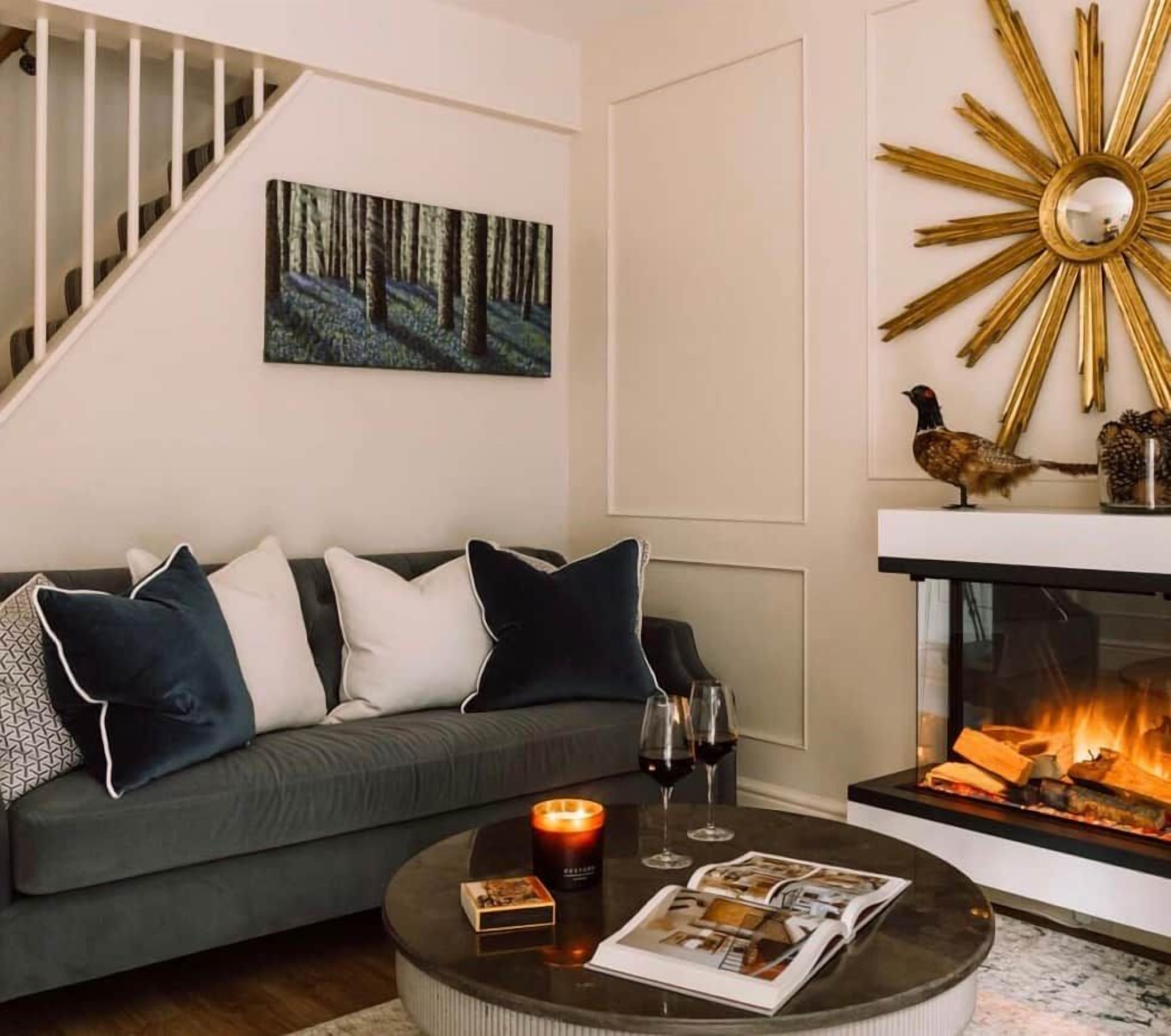 A living room with a sofa, a coffee table with magazines and a candle, a fireplace with a bird decoration, and a painting on the wall.