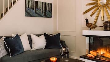 A living room with a sofa, a coffee table with magazines and a candle, a fireplace with a bird decoration, and a painting on the wall.