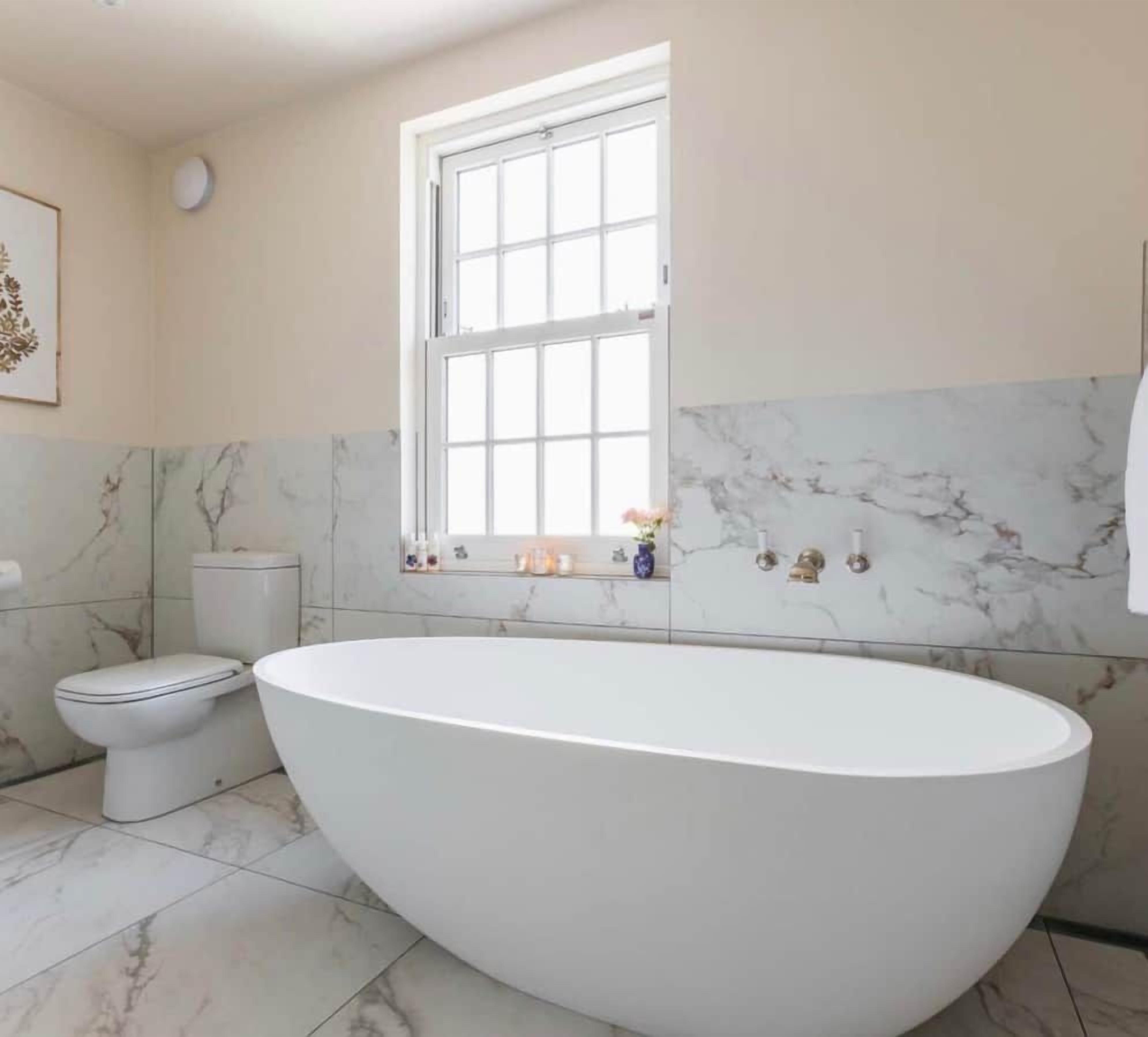 A bathroom with a freestanding bathtub, a toilet, and a window.