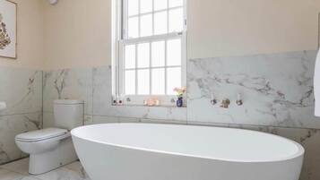A bathroom with a freestanding bathtub, a toilet, and a window.