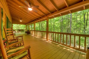 A covered porch with wooden railings, a ceiling fan, and a view of a forest. - Chestnut Bearcation - Pet-Friendly, Screened Porch, Game Room, Wood-Burning Fireplace & More! (Blue Ridge)