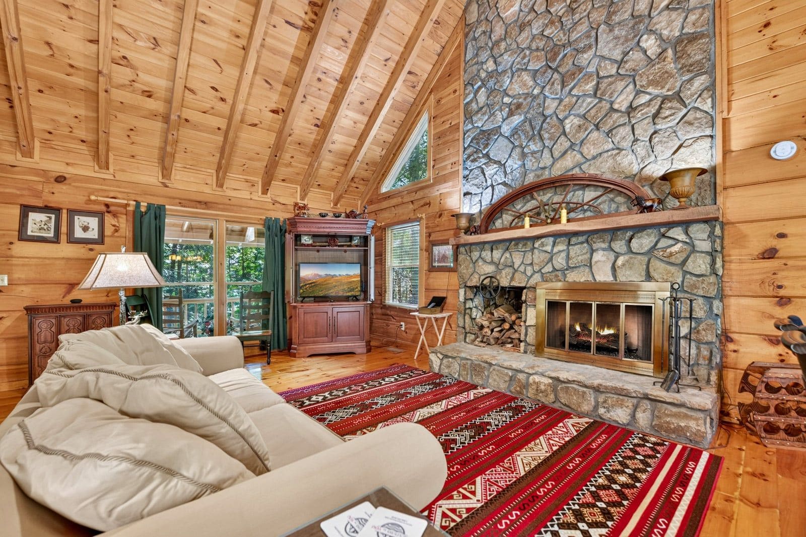 L’intérieur d’un chalet confortable, avec des murs en rondins de bois, une cheminée en pierre, un canapé confortable et un téléviseur dans le salon.