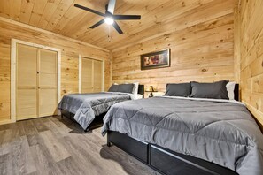 A room with two beds, wooden walls, a ceiling fan, and a framed picture on the wall. - Chestnut Bearcation - Pet-Friendly, Screened Porch, Game Room, Wood-Burning Fireplace & More! (Blue Ridge)