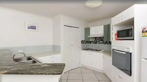 A modern kitchen with white cabinets, a granite countertop, a built-in microwave, and a stove. - Grand Florida at Miami Beach (Gold Coast)