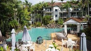 A pool area with lounge chairs and umbrellas, surrounded by palm trees and a building with multiple balconies. - Grand Florida at Miami Beach (Gold Coast)