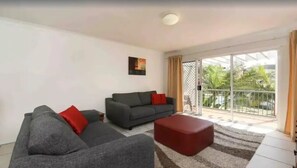 Un salon avec deux canapés, un pouf rouge et une grande porte-fenêtre coulissante donnant sur un balcon.
