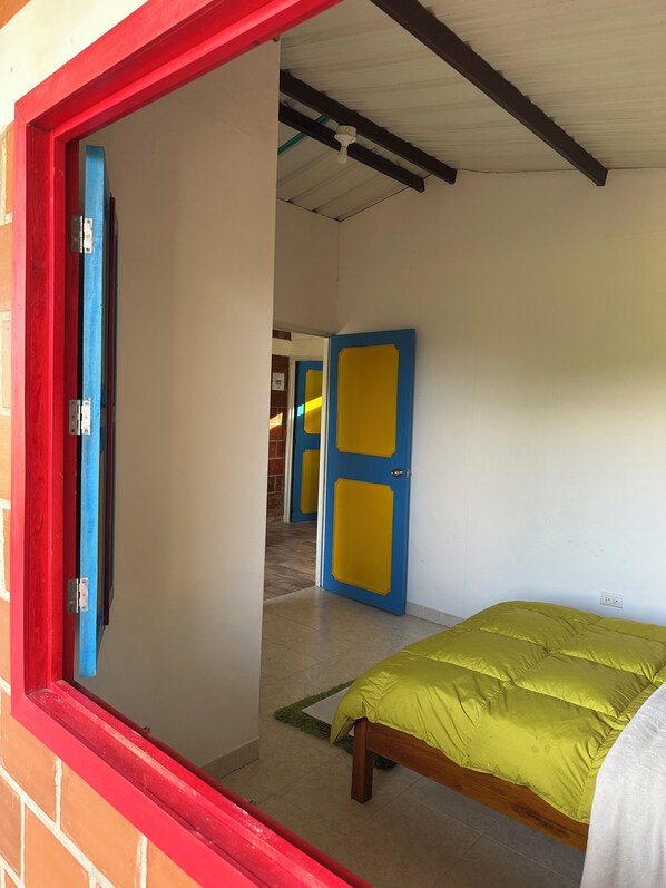 A room with a bed, a window with a red frame, and a door with blue and yellow panels.