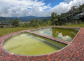 A pool with a tiled border, surrounded by greenery and a mountainous landscape in the background.