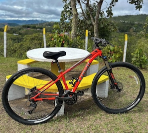 A red mountain bike parked on a concrete bench with a grassy area and trees in the background. - A cabin nestled among the mountains, birds, and a magical view in El Queremal (Valle del Cauca)