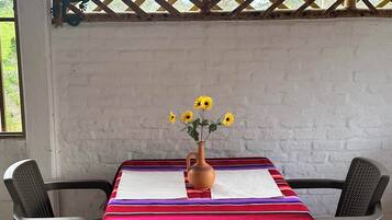 Une table recouverte d’une nappe rayée aux couleurs vives, deux chaises et un vase rempli de fleurs jaunes.