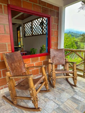 A room with two wooden rocking chairs, a brick wall, and a window with a view of greenery. - A cabin nestled among the mountains, birds, and a magical view in El Queremal (Valle del Cauca)